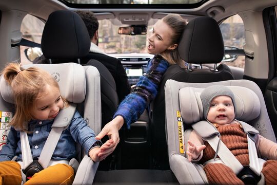 Imagebild: Frau auf Beifahrersitz im Auto kümmert sich um Kind auf den Rücksitzen