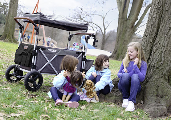 Kinder sitzen an einem Baum, im Hintergrund ein Bollerwagen der Firma Keenz